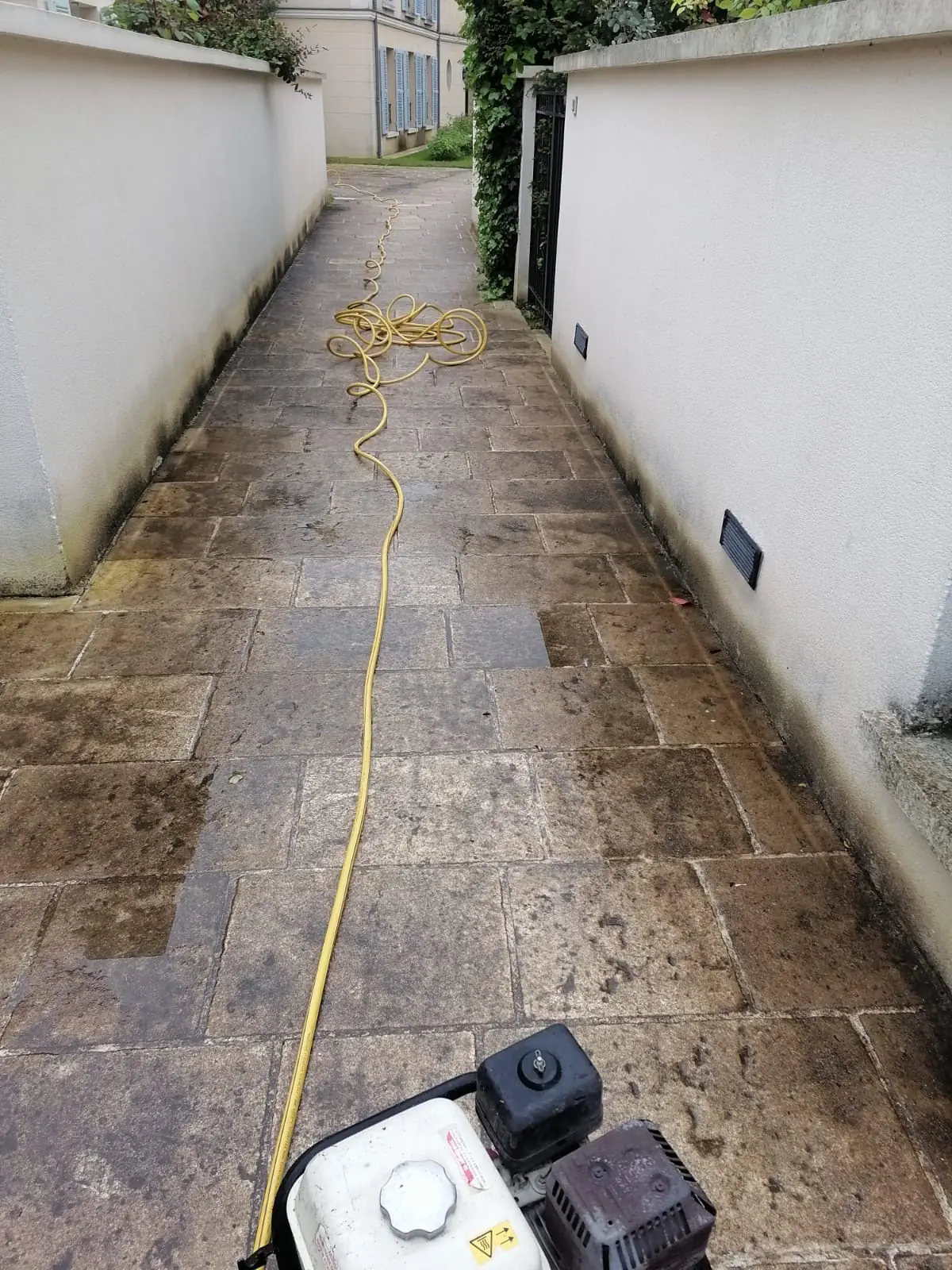 Allée en pierre entre deux murs blancs, en cours de lavage, le nettoyeur au premier plan