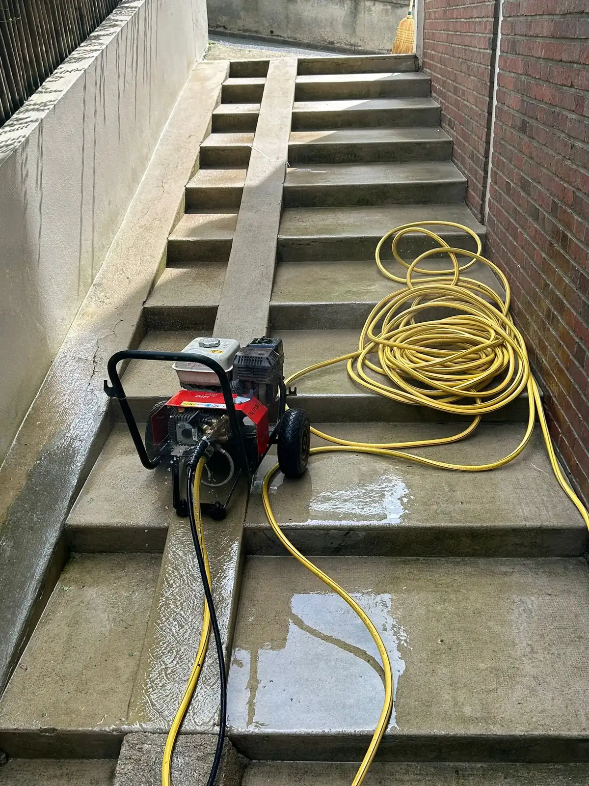 Escalier extérieur en béton en cours de lavage, le nettoyeur haute pression et son tuyau jaune posés sur les marches